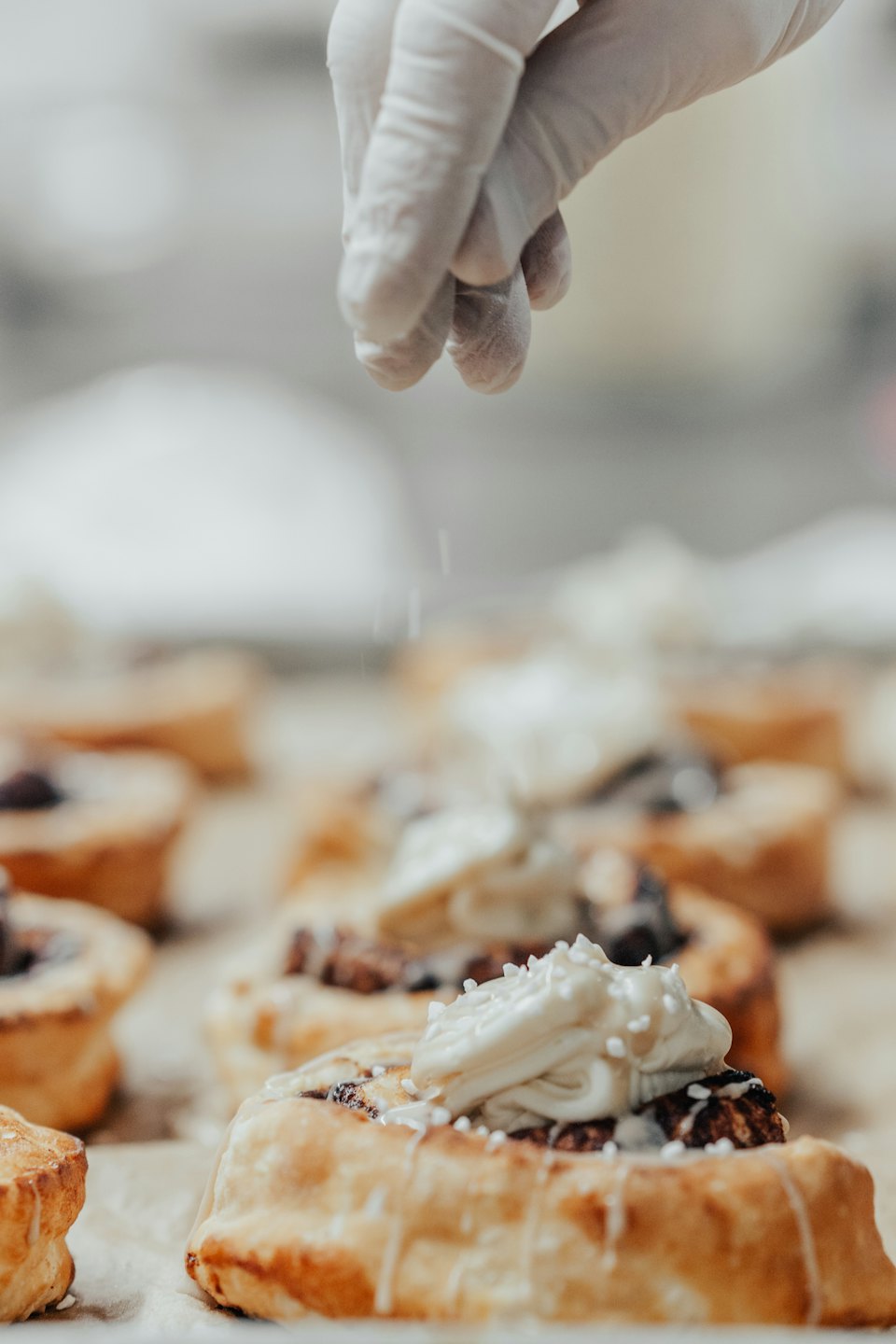 A gloved hand sprinkles white toppings onto a frosted pastry.