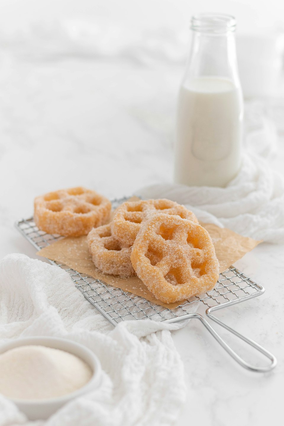 Golden, sugar-coated fried pastries on a cooling rack with milk.